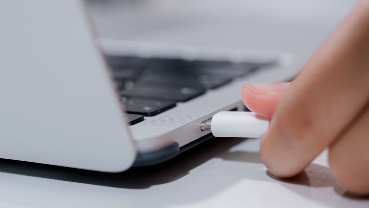 Person's hand about to plug ta USB Type-C cable into the laptop’s charging port. 