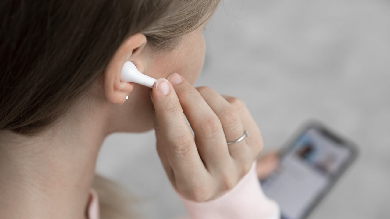 Person plugging earbuds to her ear with smartphone in another hand