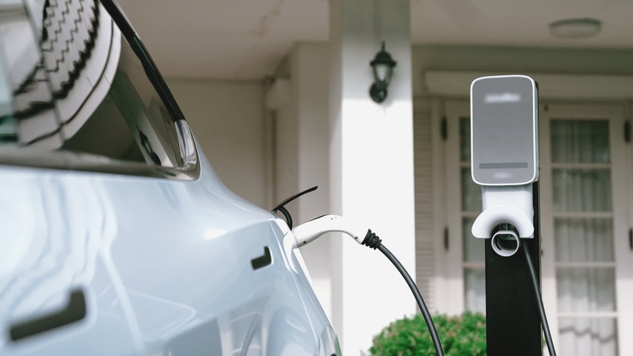 White electric car connected to an EV charging station outside a residential home.